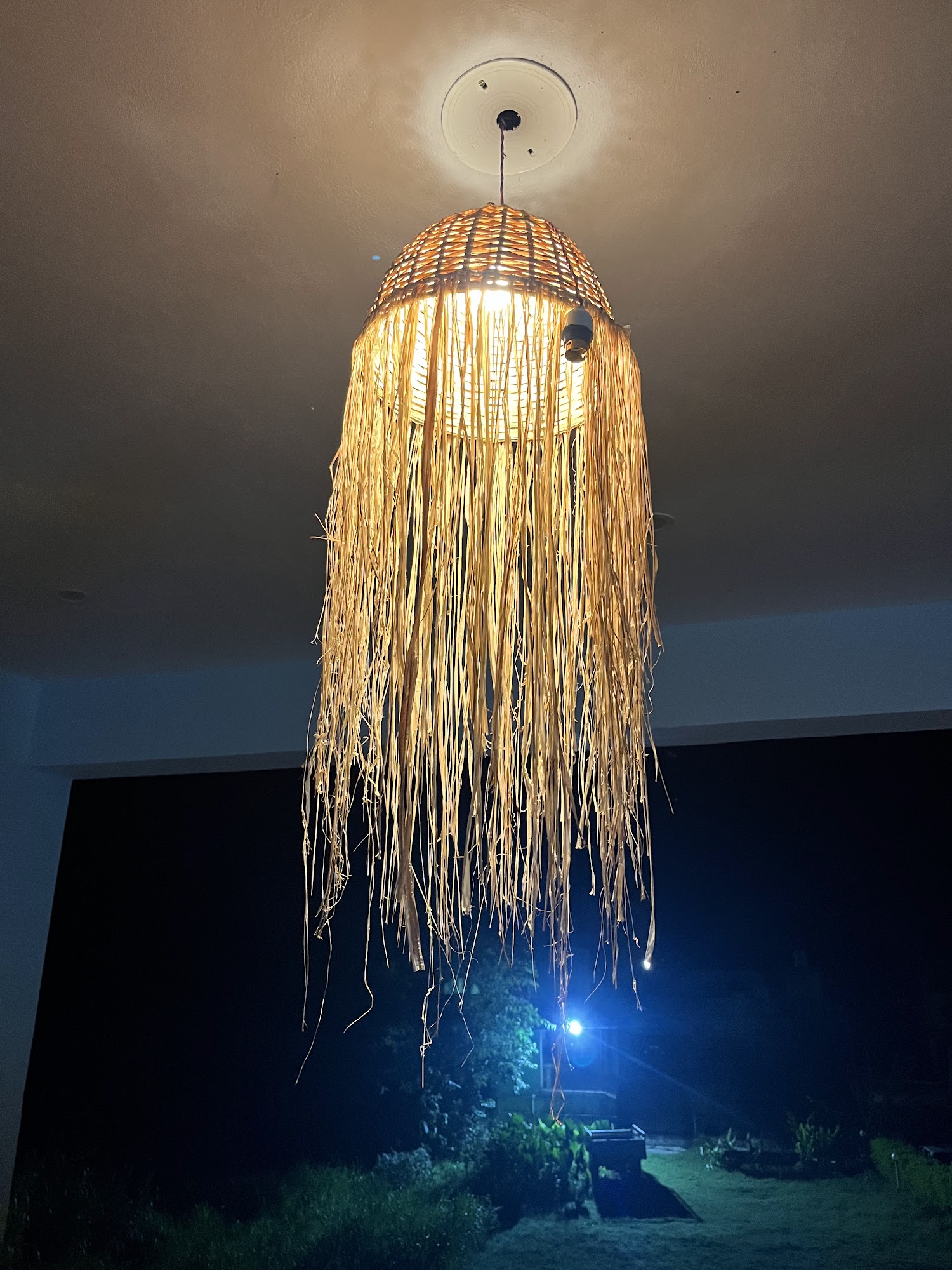 Handwoven pendant lamp glowing softly at dusk